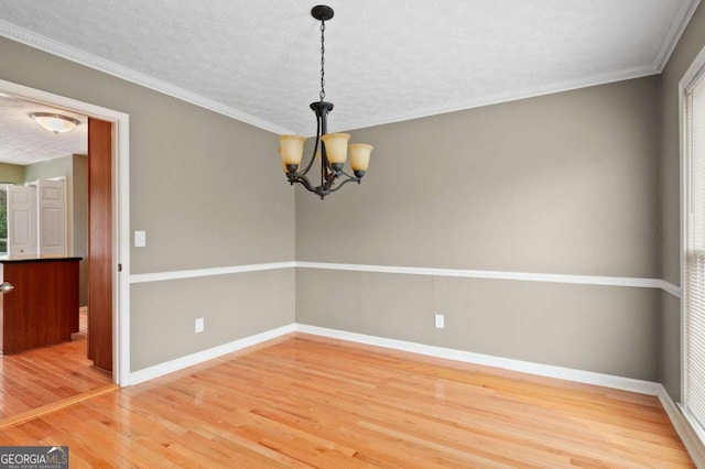 spare room with a textured ceiling, an inviting chandelier, ornamental molding, and hardwood / wood-style flooring