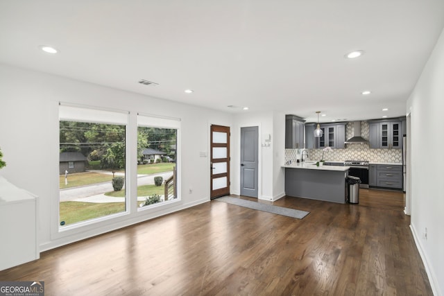 kitchen featuring high end stainless steel range, decorative backsplash, dark wood-type flooring, wall chimney exhaust hood, and gray cabinetry