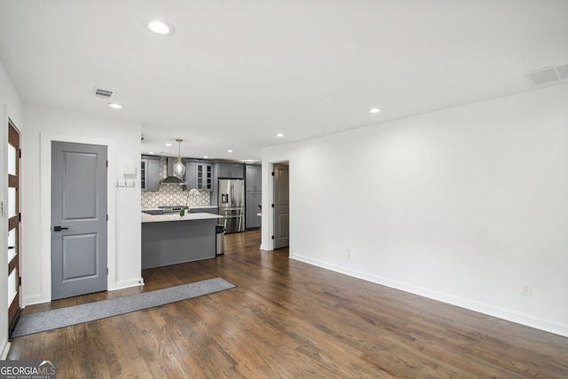 kitchen with dark hardwood / wood-style floors, stainless steel fridge, wall chimney exhaust hood, decorative light fixtures, and tasteful backsplash