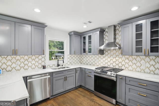 kitchen with dark hardwood / wood-style floors, light stone countertops, appliances with stainless steel finishes, sink, and wall chimney range hood