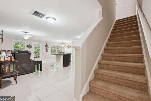 stairway with ornamental molding, ceiling fan with notable chandelier, and tile patterned floors