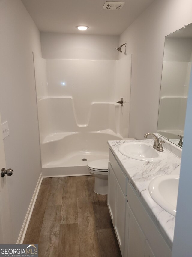 bathroom with hardwood / wood-style floors, a shower, double sink vanity, and toilet