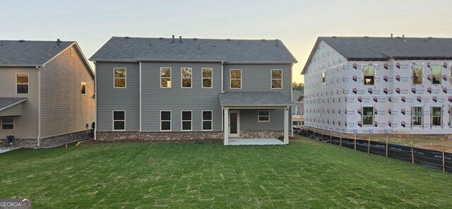 back house at dusk featuring a patio and a lawn