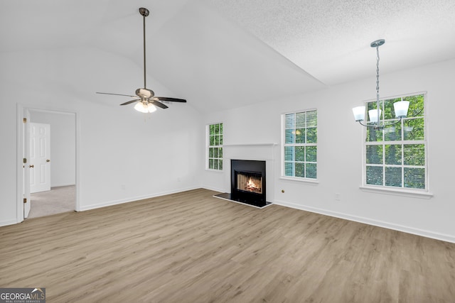 unfurnished living room with high vaulted ceiling, ceiling fan with notable chandelier, a textured ceiling, and light hardwood / wood-style floors