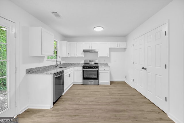 kitchen with sink, appliances with stainless steel finishes, light stone countertops, light hardwood / wood-style floors, and white cabinets