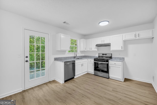 kitchen with sink, appliances with stainless steel finishes, white cabinetry, light stone counters, and light wood-type flooring