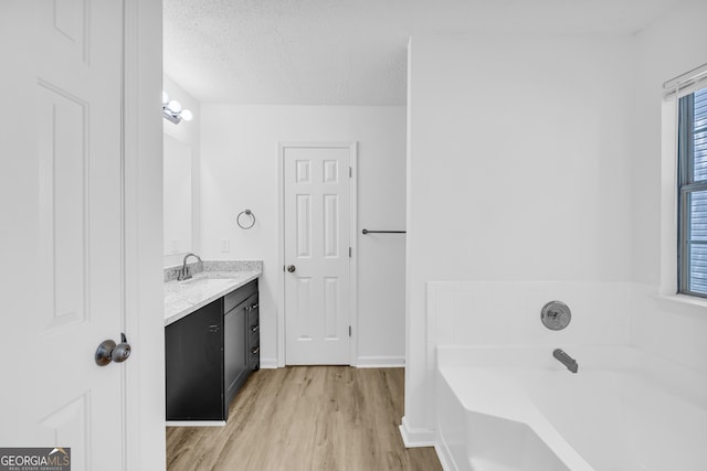 bathroom with vanity, hardwood / wood-style floors, a textured ceiling, and a tub to relax in