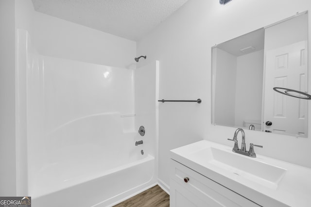 full bathroom with hardwood / wood-style floors, vanity, toilet, a textured ceiling, and washtub / shower combination