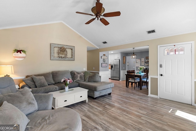 living area featuring ceiling fan, lofted ceiling, light wood-style flooring, visible vents, and ornamental molding