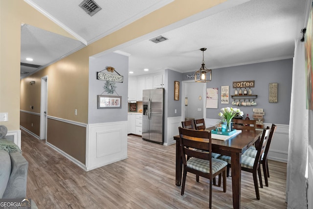 dining room with wainscoting, visible vents, crown molding, and light wood-style flooring