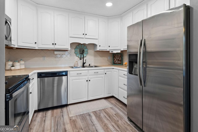 kitchen with light wood finished floors, a sink, stainless steel appliances, white cabinets, and light countertops