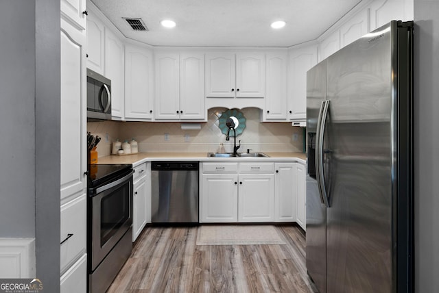 kitchen with appliances with stainless steel finishes, a sink, visible vents, and white cabinetry