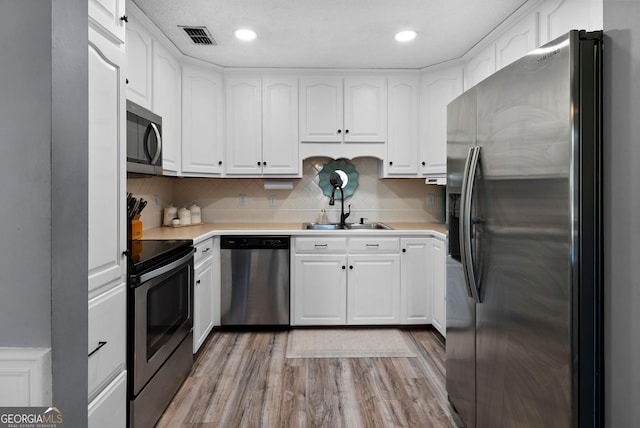 kitchen with visible vents, light wood-style flooring, a sink, appliances with stainless steel finishes, and white cabinetry