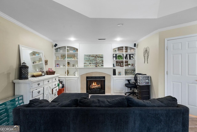 living room featuring wood finished floors, ornamental molding, a tile fireplace, and built in shelves