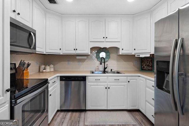 kitchen with stainless steel appliances, wood finished floors, a sink, white cabinetry, and decorative backsplash