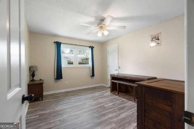 home office with ceiling fan, a textured ceiling, baseboards, and wood finished floors