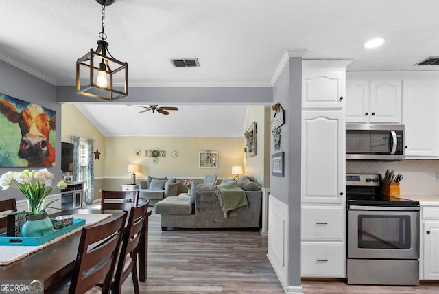 kitchen featuring a ceiling fan, light wood-style floors, white cabinets, appliances with stainless steel finishes, and decorative light fixtures