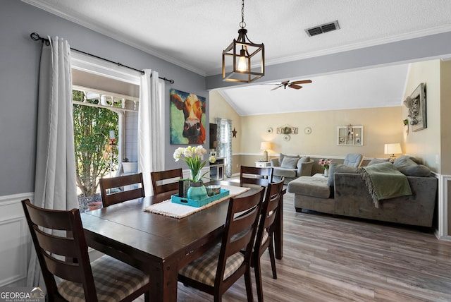 dining space featuring wood finished floors, visible vents, ornamental molding, ceiling fan, and vaulted ceiling