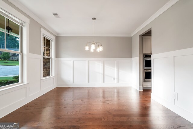 unfurnished dining area with hardwood / wood-style floors, ornamental molding, and a notable chandelier