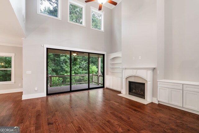 unfurnished living room featuring ceiling fan, dark wood-type flooring, a towering ceiling, and plenty of natural light