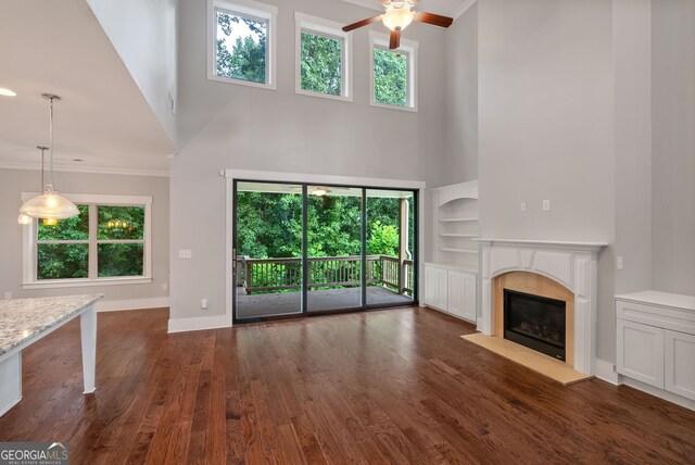 unfurnished living room featuring ornamental molding, dark hardwood / wood-style flooring, ceiling fan, and a high ceiling