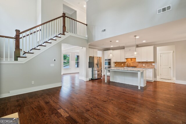 kitchen featuring a center island with sink, dark hardwood / wood-style flooring, pendant lighting, appliances with stainless steel finishes, and white cabinets