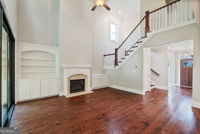 unfurnished living room featuring built in features, ceiling fan, ornamental molding, a towering ceiling, and hardwood / wood-style flooring