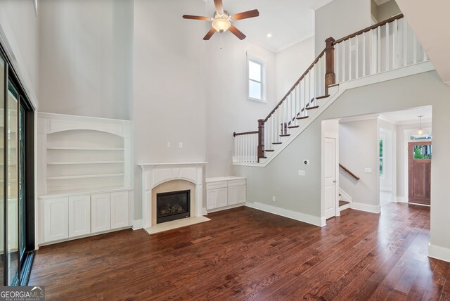 unfurnished living room featuring ceiling fan, a towering ceiling, hardwood / wood-style flooring, a fireplace, and built in features