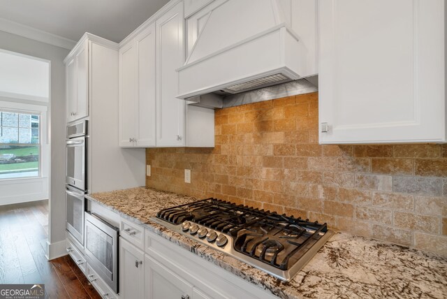 kitchen featuring appliances with stainless steel finishes, white cabinets, custom range hood, backsplash, and dark hardwood / wood-style flooring