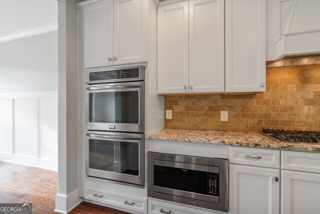 kitchen featuring stainless steel appliances, white cabinetry, backsplash, wood-type flooring, and custom range hood