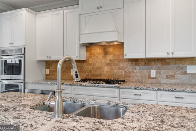 kitchen featuring appliances with stainless steel finishes, white cabinets, custom range hood, backsplash, and sink