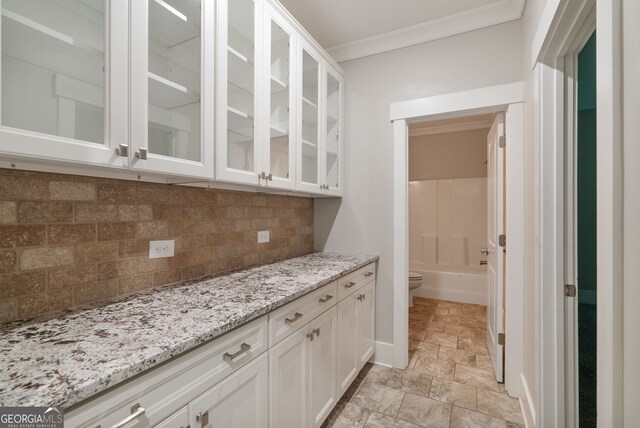 kitchen featuring light tile patterned floors, white cabinets, light stone countertops, tasteful backsplash, and ornamental molding