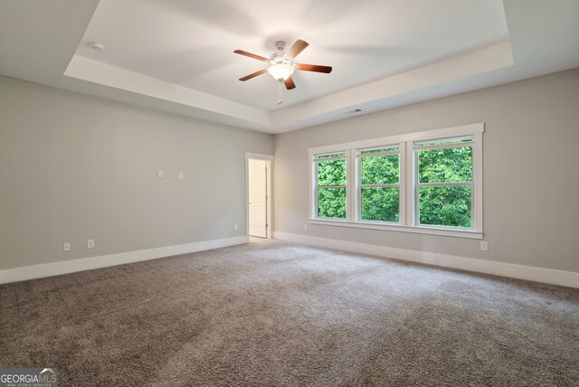 empty room featuring a tray ceiling, carpet flooring, and ceiling fan