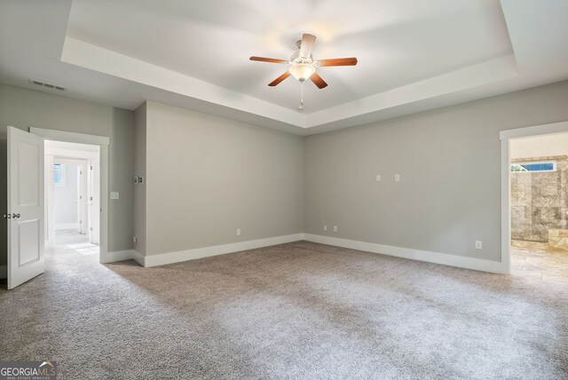 empty room with ceiling fan, a tray ceiling, and light carpet