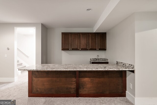 kitchen with dark brown cabinetry, kitchen peninsula, light carpet, and light stone countertops