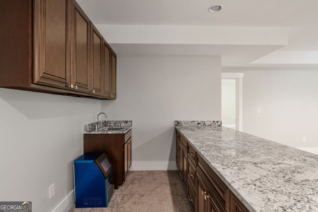 kitchen featuring light carpet, dark brown cabinets, light stone counters, and sink