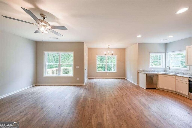 unfurnished living room with sink, ceiling fan with notable chandelier, and light hardwood / wood-style floors