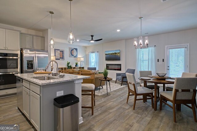 kitchen featuring ceiling fan with notable chandelier, appliances with stainless steel finishes, light wood-type flooring, sink, and light stone counters