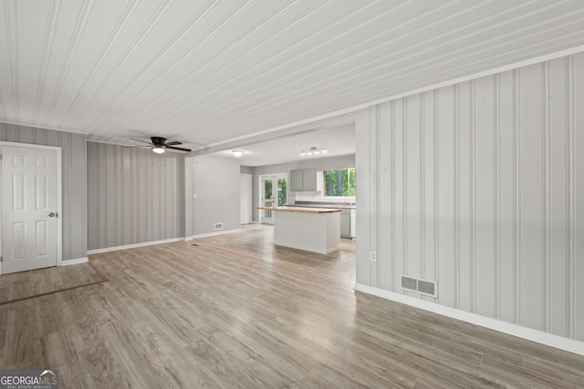 unfurnished living room with light hardwood / wood-style flooring, wooden walls, and ceiling fan