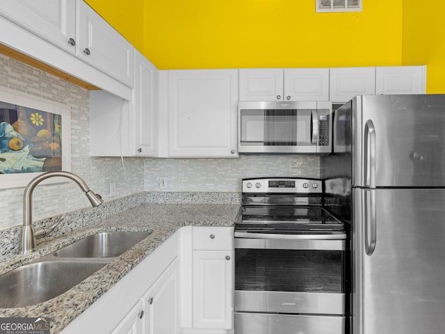 kitchen with light stone counters, appliances with stainless steel finishes, white cabinets, backsplash, and sink