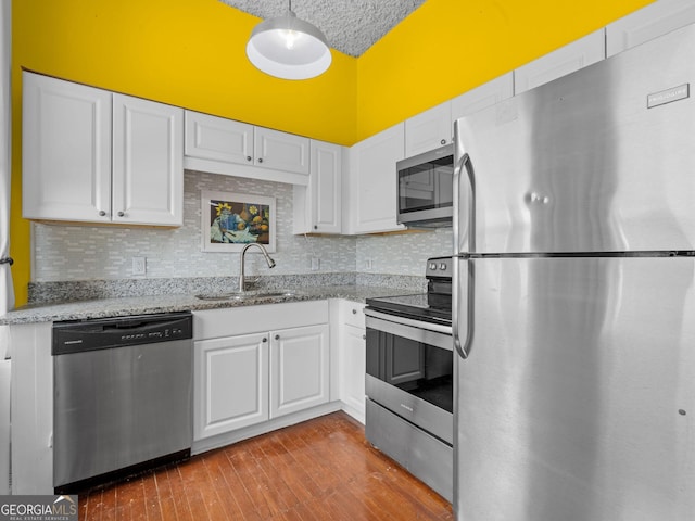 kitchen with stainless steel appliances, white cabinets, backsplash, sink, and hardwood / wood-style flooring