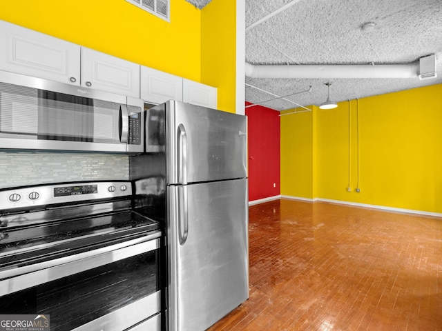 kitchen with decorative backsplash, a textured ceiling, white cabinetry, appliances with stainless steel finishes, and hardwood / wood-style flooring