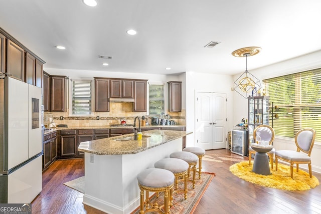 kitchen featuring decorative backsplash, hardwood / wood-style floors, sink, a center island with sink, and white fridge with ice dispenser