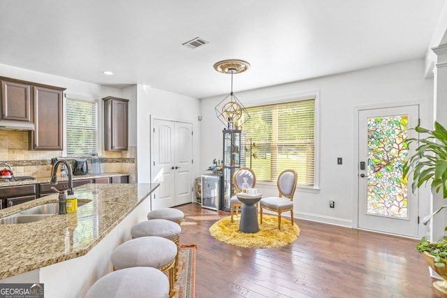 interior space featuring decorative backsplash, dark hardwood / wood-style floors, hanging light fixtures, light stone countertops, and sink