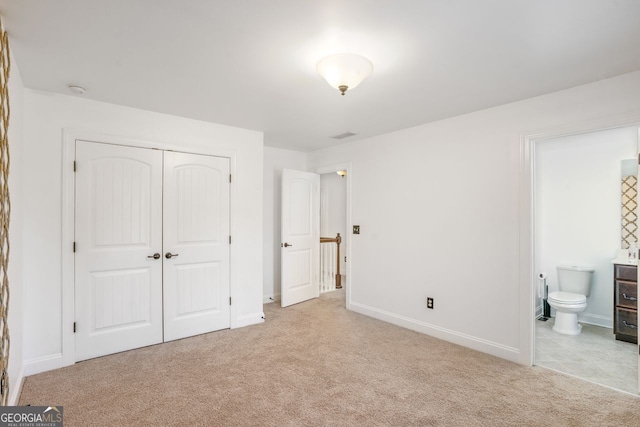 unfurnished bedroom with ensuite bath, a closet, and light carpet