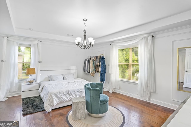 bedroom with a chandelier, hardwood / wood-style flooring, a tray ceiling, and multiple windows