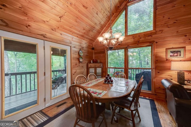 dining room with high vaulted ceiling, a wealth of natural light, an inviting chandelier, and hardwood / wood-style flooring