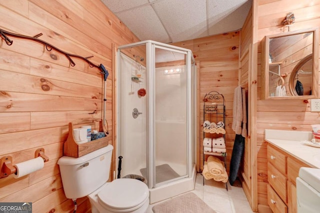 bathroom featuring toilet, wood walls, a drop ceiling, walk in shower, and vanity