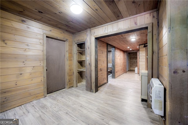 corridor with heating unit, a barn door, wood walls, wooden ceiling, and light hardwood / wood-style flooring