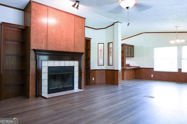 unfurnished living room featuring a tile fireplace, dark hardwood / wood-style flooring, vaulted ceiling, a textured ceiling, and ornamental molding